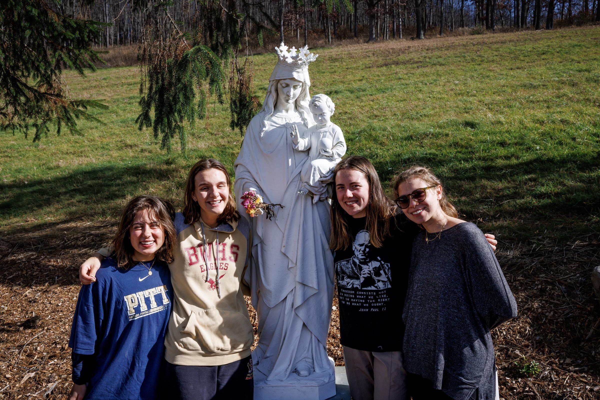 Students embrace beside a Marian statue outdoors